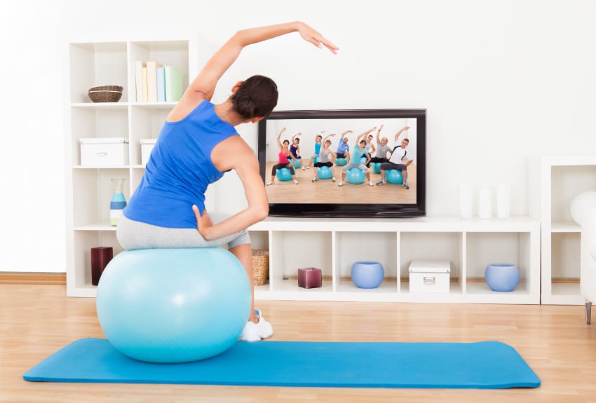 Woman working out on an exercise ball at home instead of at a pilates studio