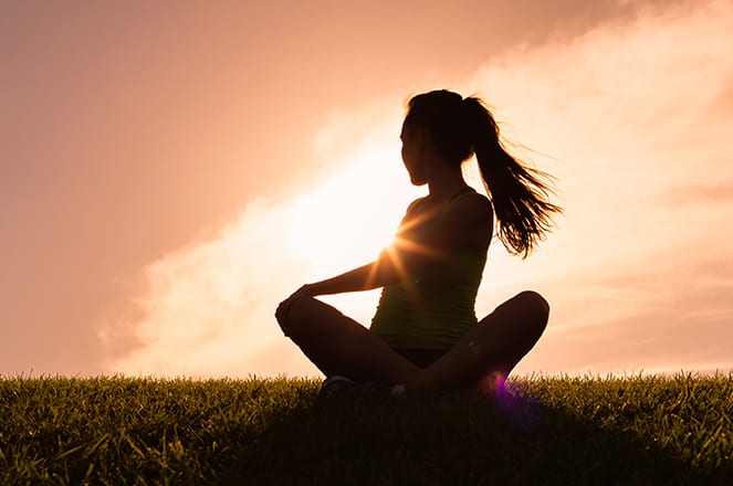Woman sitting in the grass exercising a balanced body with a sunset